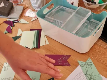 Colourful pieces of paper lie on a table; hand moves.