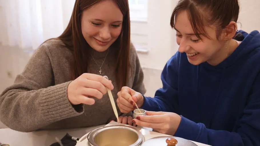 Two women making candles at a table.