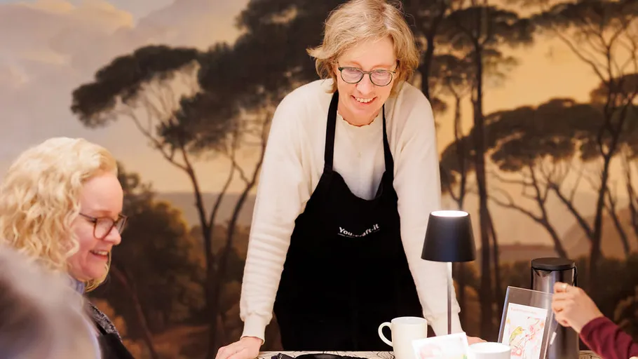 Frau in Schürze lächelt am Tisch mit anderen.
