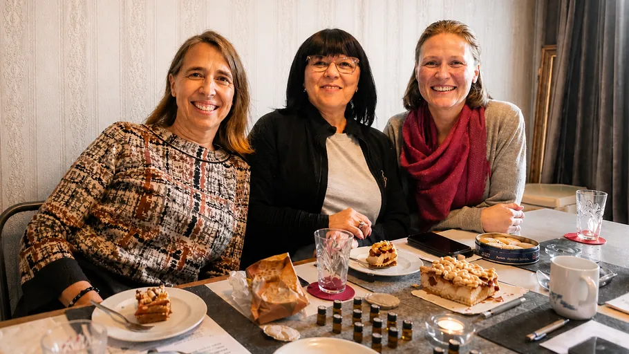 Drei Frauen lächeln an einem Tisch mit Kuchen.