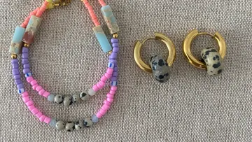 Farbenfrohe Perlenkette und goldene Ohrringe auf Stoff.