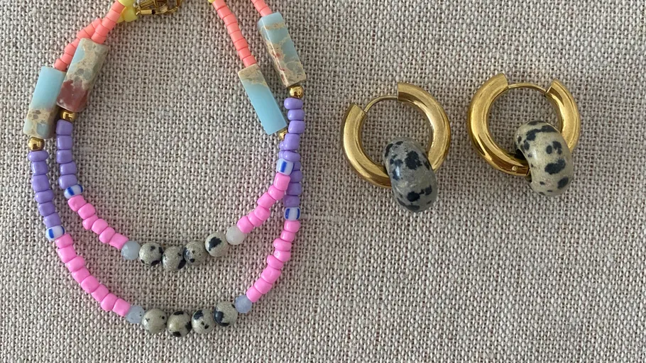 Colorful beaded necklace and gold earrings on fabric.