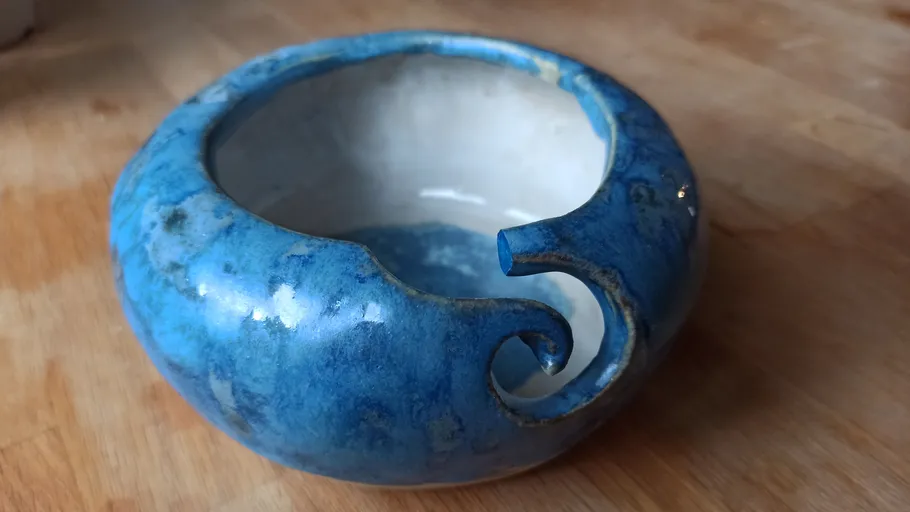Blue ceramic yarn bowl on wooden surface.