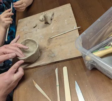 Hands sculpting clay on a wooden board.