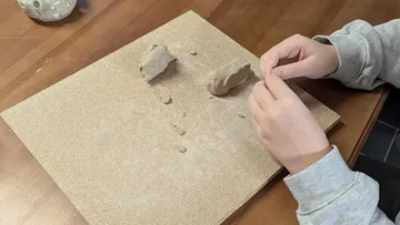 Hands sculpting clay on a board.