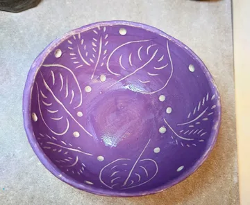 Purple bowl with leaf patterns, resting on table.