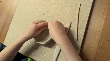 Hands shaping clay on a wooden table.