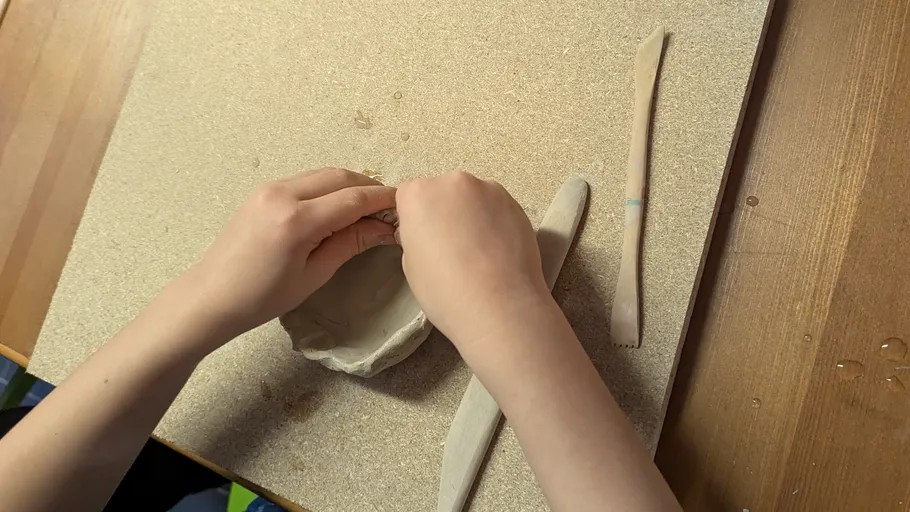Hands shaping clay on a wooden table.