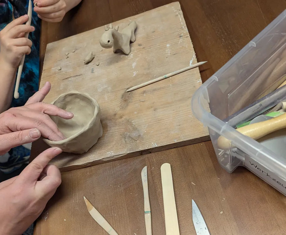 Hands sculpting clay bowl with tools nearby.