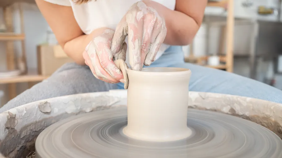 Hands shaping clay on pottery wheel indoors.