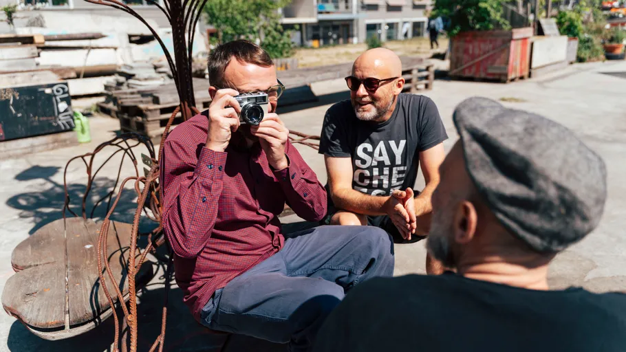 Drei Männer im Freien, einer fotografiert.