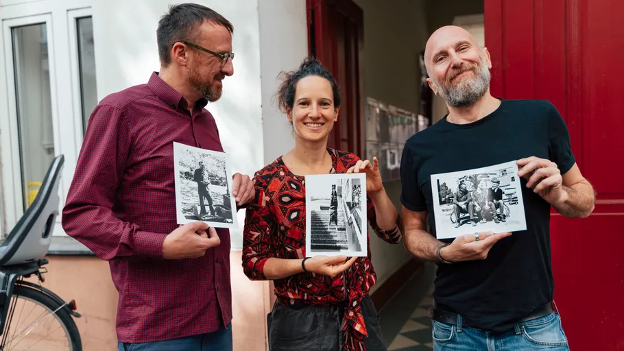 Three people holding black-and-white photos outdoors.