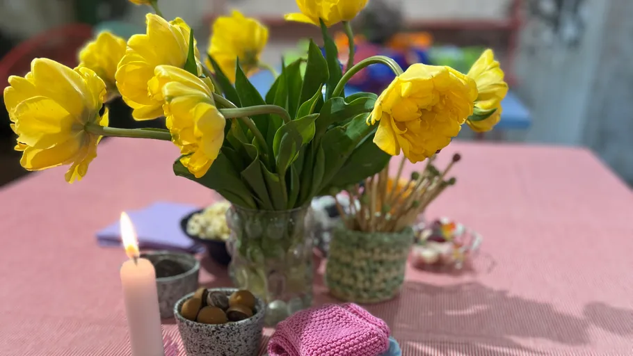 Gelbe Blumen in Vase, Kerze auf Tisch.