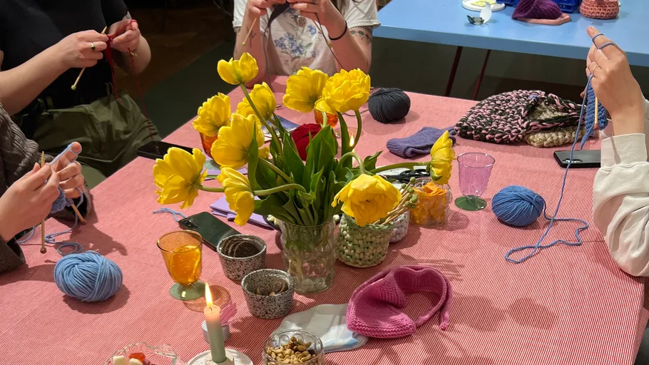 Personen stricken an einem Tisch mit Blumen.