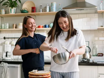 Two laughing women bake together in a kitchen.