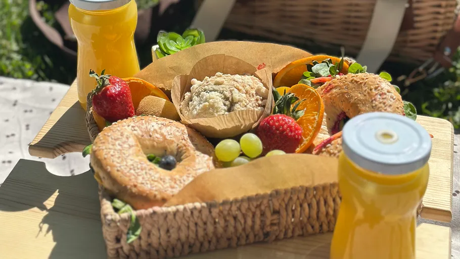Basket with bagels, fruits, and juice outdoors.
