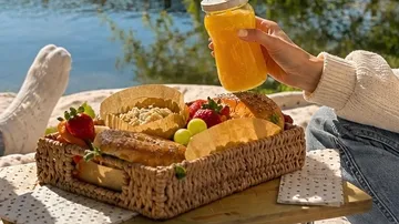 Picnic basket with food and drink by a lake.