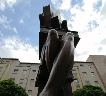 Skulptur von verschlungenen Beinen vor wolkigem Himmel.