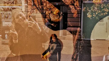 Personen spiegeln sich im Fenster mit Baumüberlagerung.