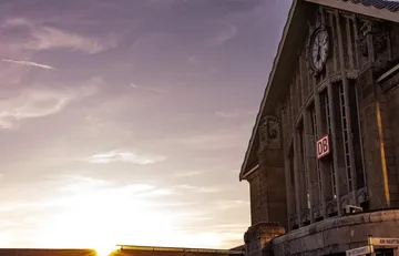Bahnhof-Außenansicht mit Uhr bei Sonnenuntergang.