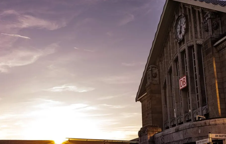 Bahnhof-Außenansicht mit Uhr bei Sonnenuntergang.