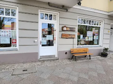 Ladenfront mit Bank und Plakaten draußen.