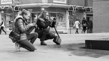 Two women taking photos in urban setting.
