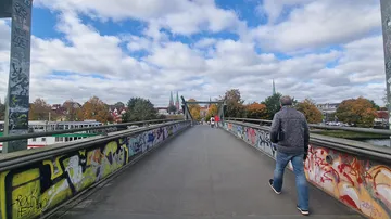 Man walking on graffiti-covered bridge, cloudy sky.
