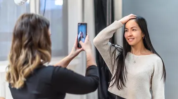 Woman photographing another woman posing indoors.