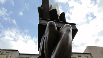 Hohe abstrakte Skulptur vor bewölktem Himmel.