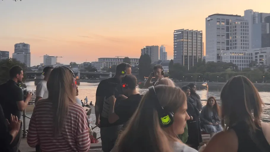 People with headphones by a riverside at sunset.
