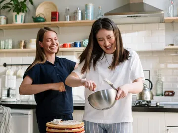 Zwei Frauen lachen beim Kochen in einer modernen Küche.