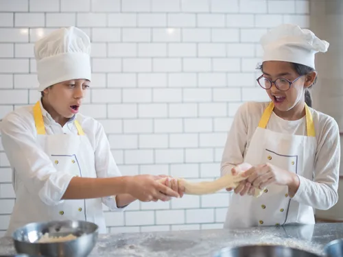Zwei Kinder dehnen Teig in einer hellen Küche.