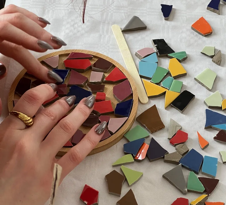 Hände ordnen bunte Mosaikfliesen auf Tisch.