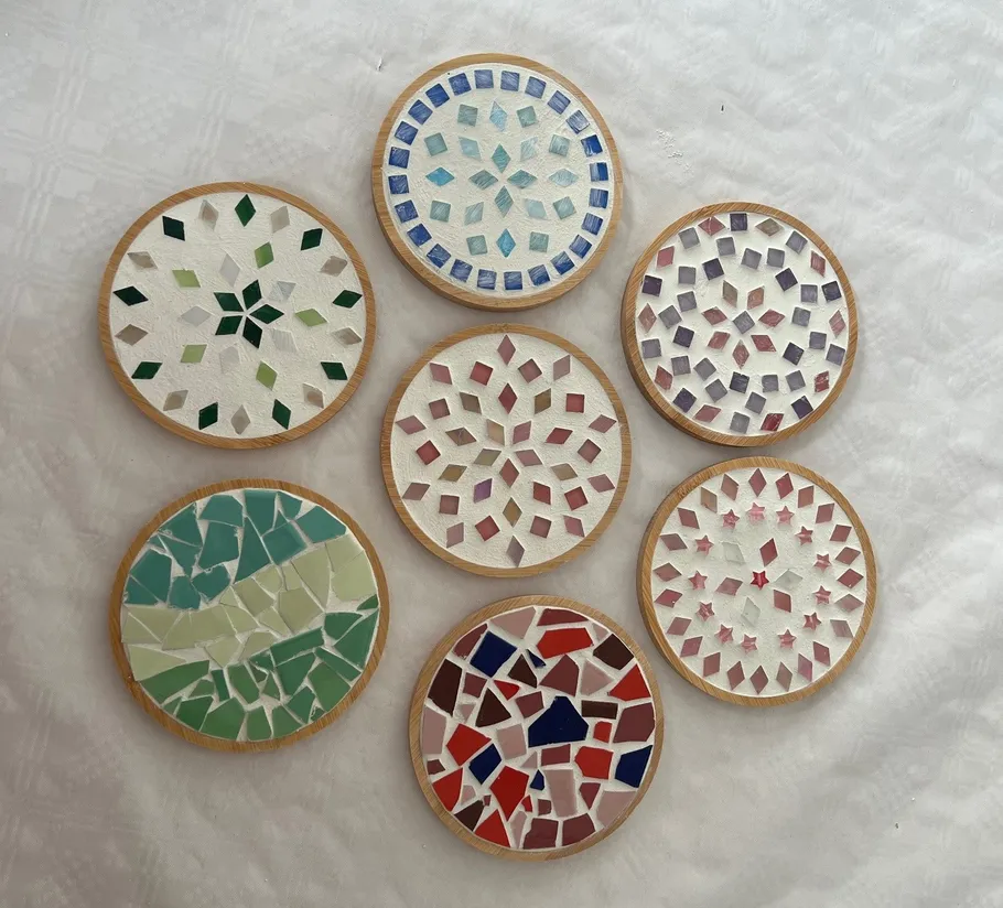 Sieben Mosaik-Untersetzer auf einer weißen Oberfläche.