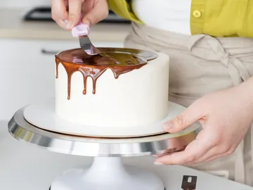 A person covers a cake with chocolaty icing.