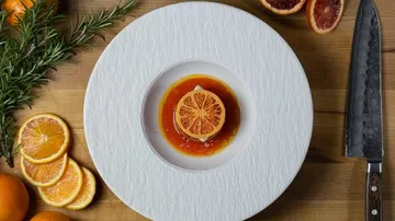Orangenscheibe in Schüssel mit Messer auf Tisch.