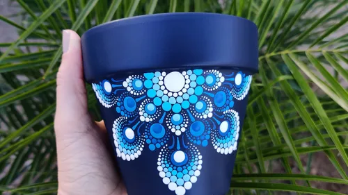 Hand hält blauen Topf mit weißen Mustern im Freien.