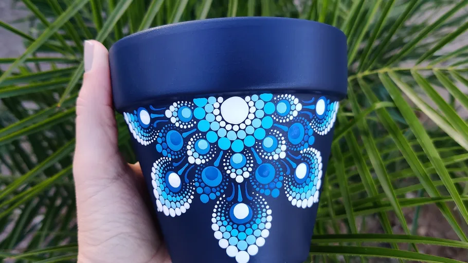 Hand hält blauen Topf mit weißen Mustern im Freien.