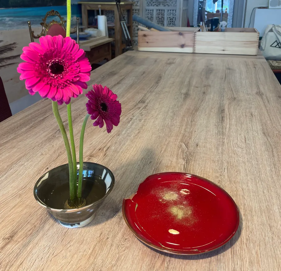 Rosa Blumen in Vase neben rotem Teller auf Tisch.