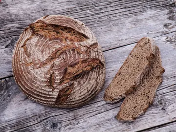 Rundes Brot liegt neben zwei geschnittenen Stücke auf Holz.
