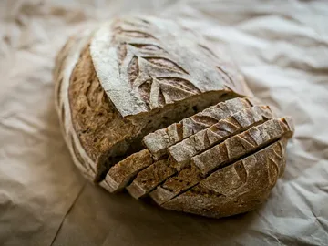 A loaf of bread, cut in half, is on brown paper.