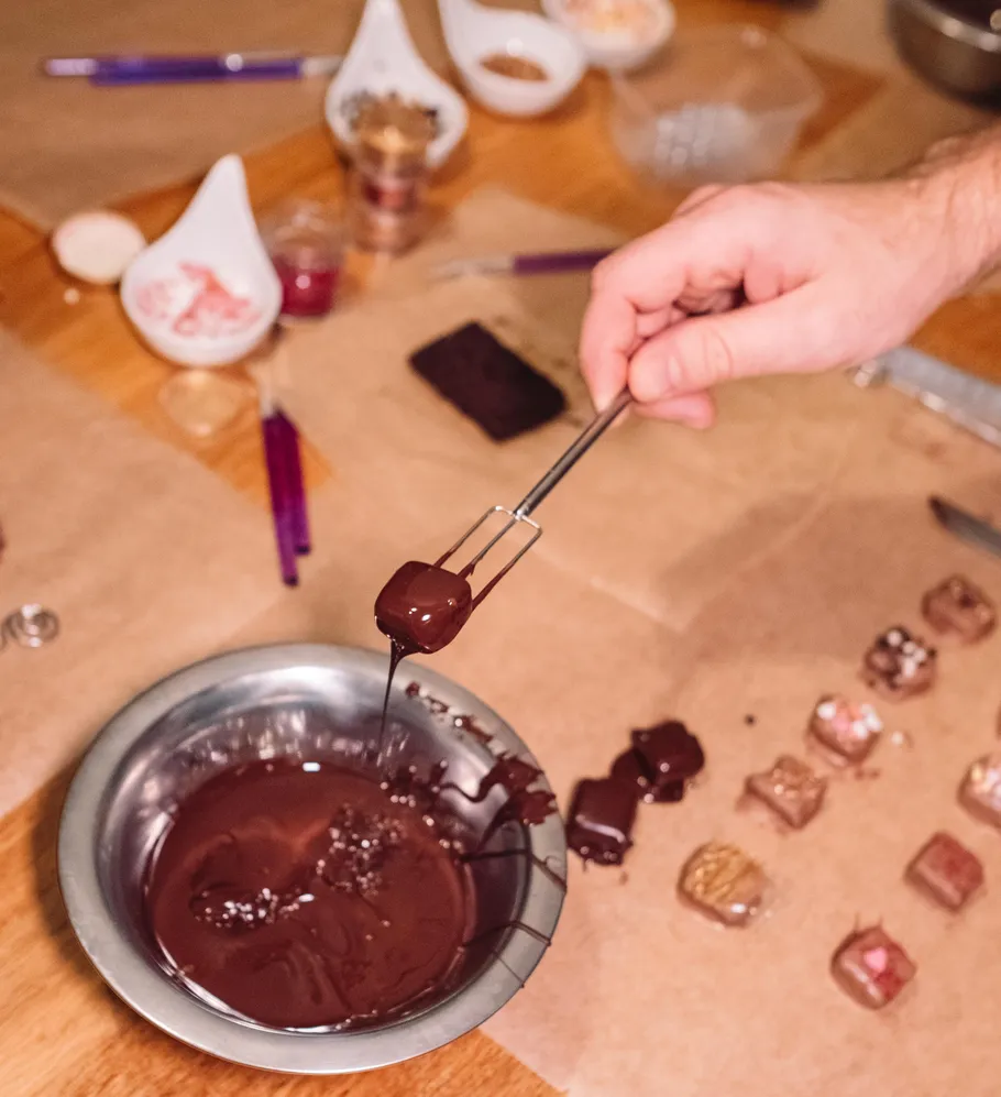 Hand taucht Praline in geschmolzene Schokolade.