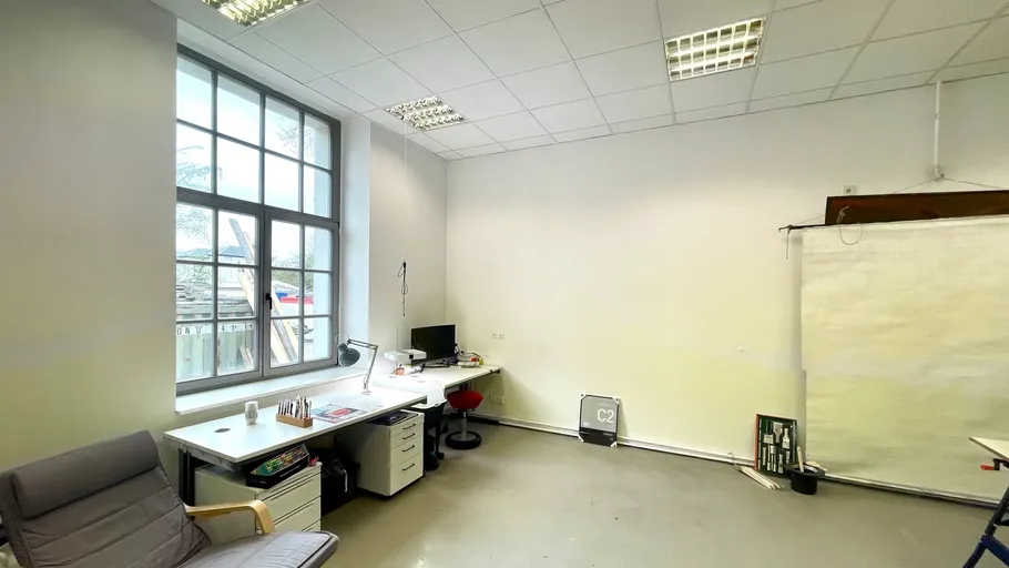Büro mit Schreibtisch, Stuhl, großes Fenster, weiße Wände.