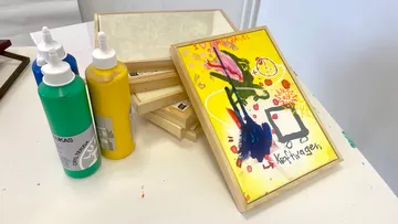Colorful abstract painting next to paint bottles.