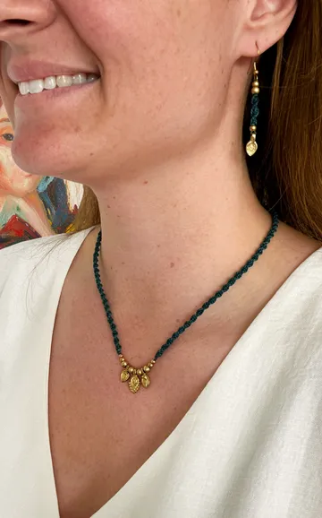 Woman wears necklace and earring with art background.