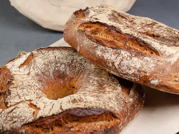 Two rustic breads lie on a bright surface.