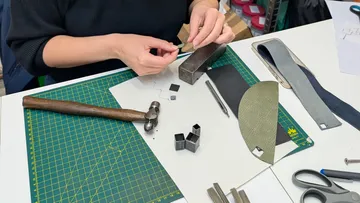 Person crafting with tools and materials on table.
