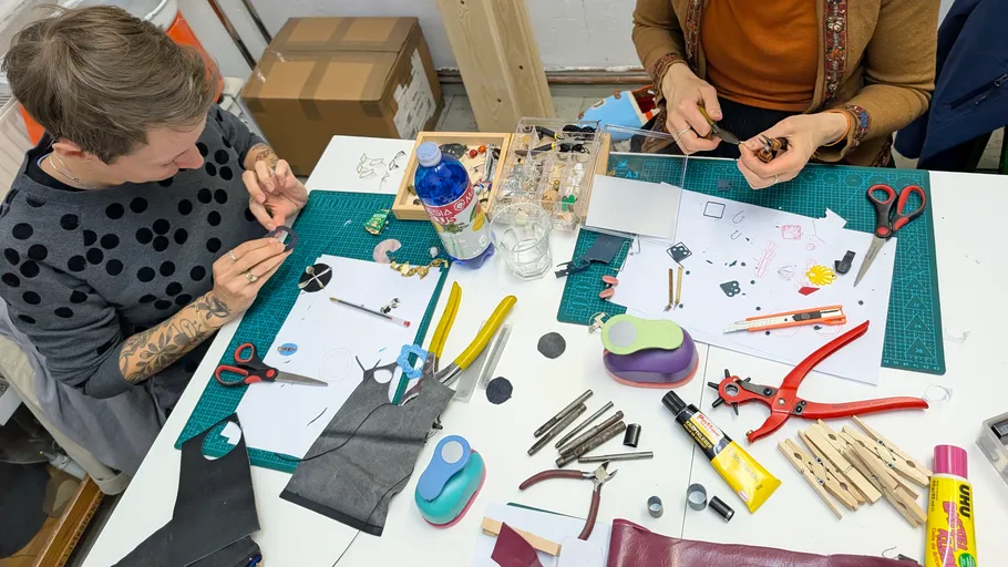 Two people crafting on a cluttered table.