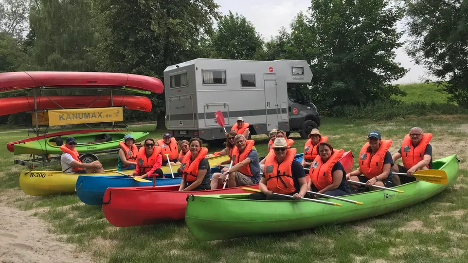 Gruppe in Kajaks mit Schwimmwesten, geparktes Wohnmobil nahebei.